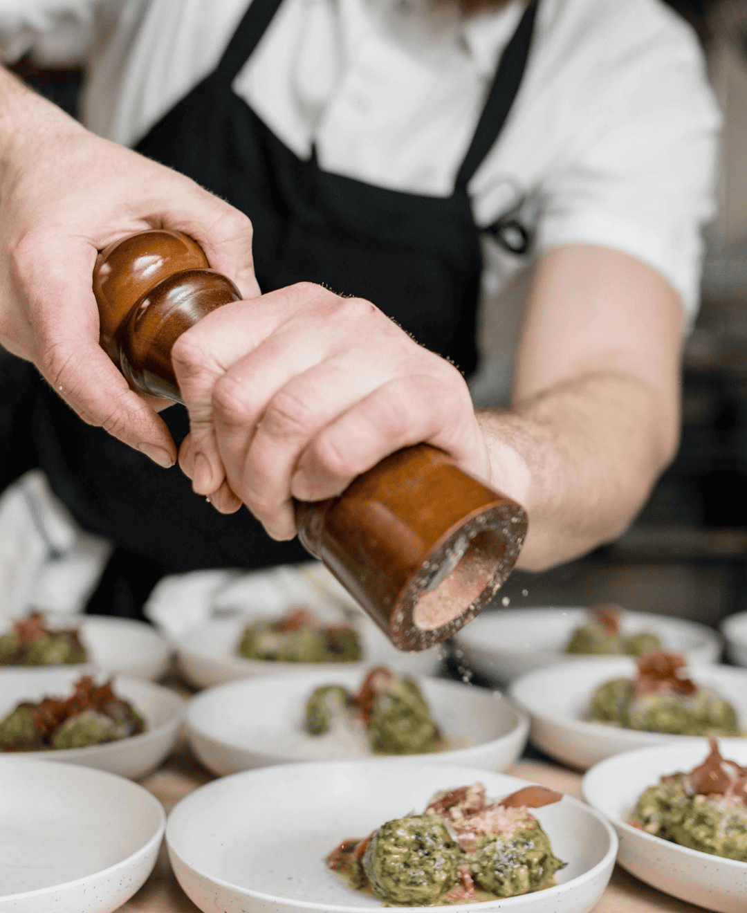 Salt grinder being used to season dishes in a busy hotel kitchen.