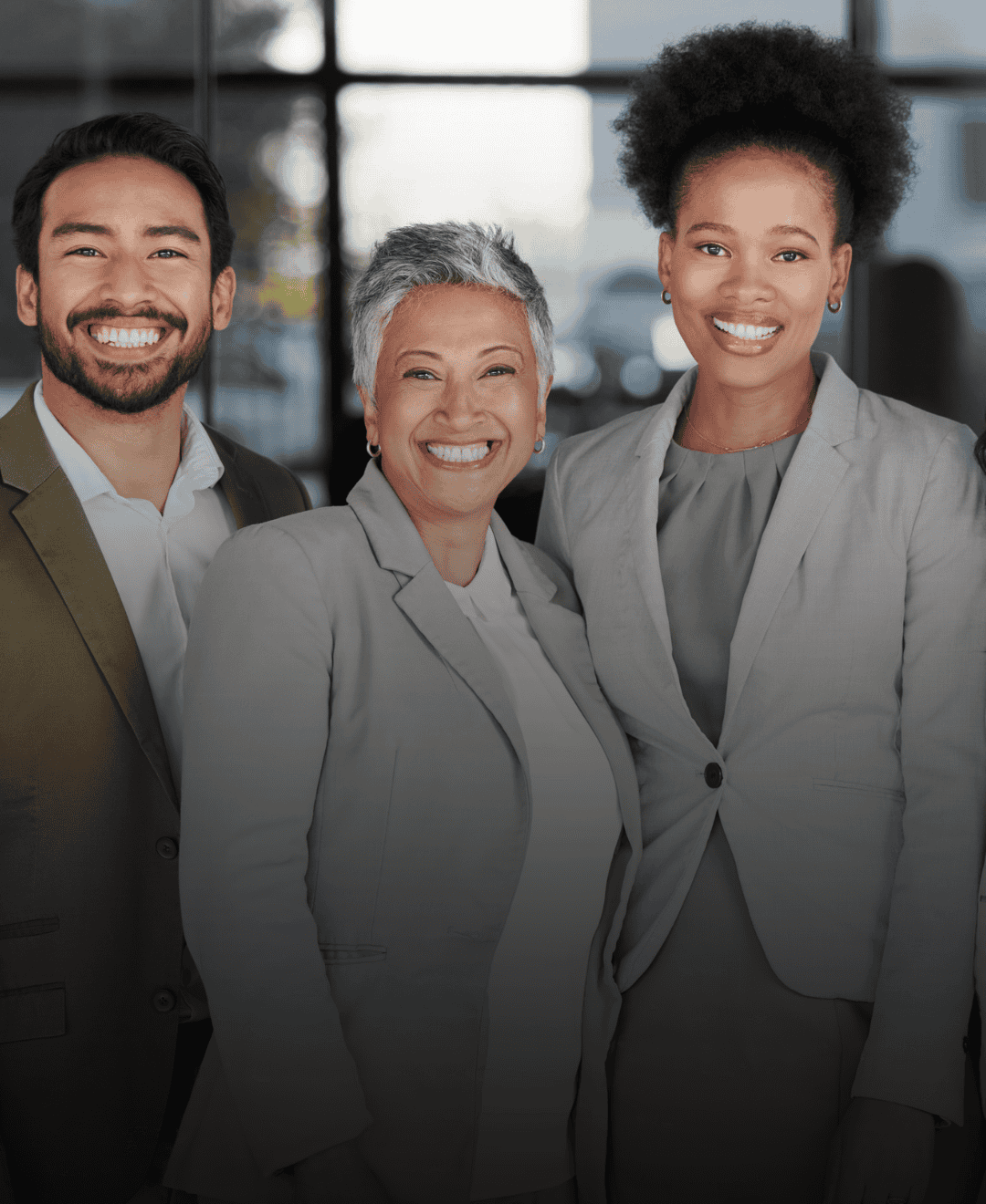 Three diverse business professionals smiling together in a modern office, representing teamwork, leadership, and workplace collaboration.
