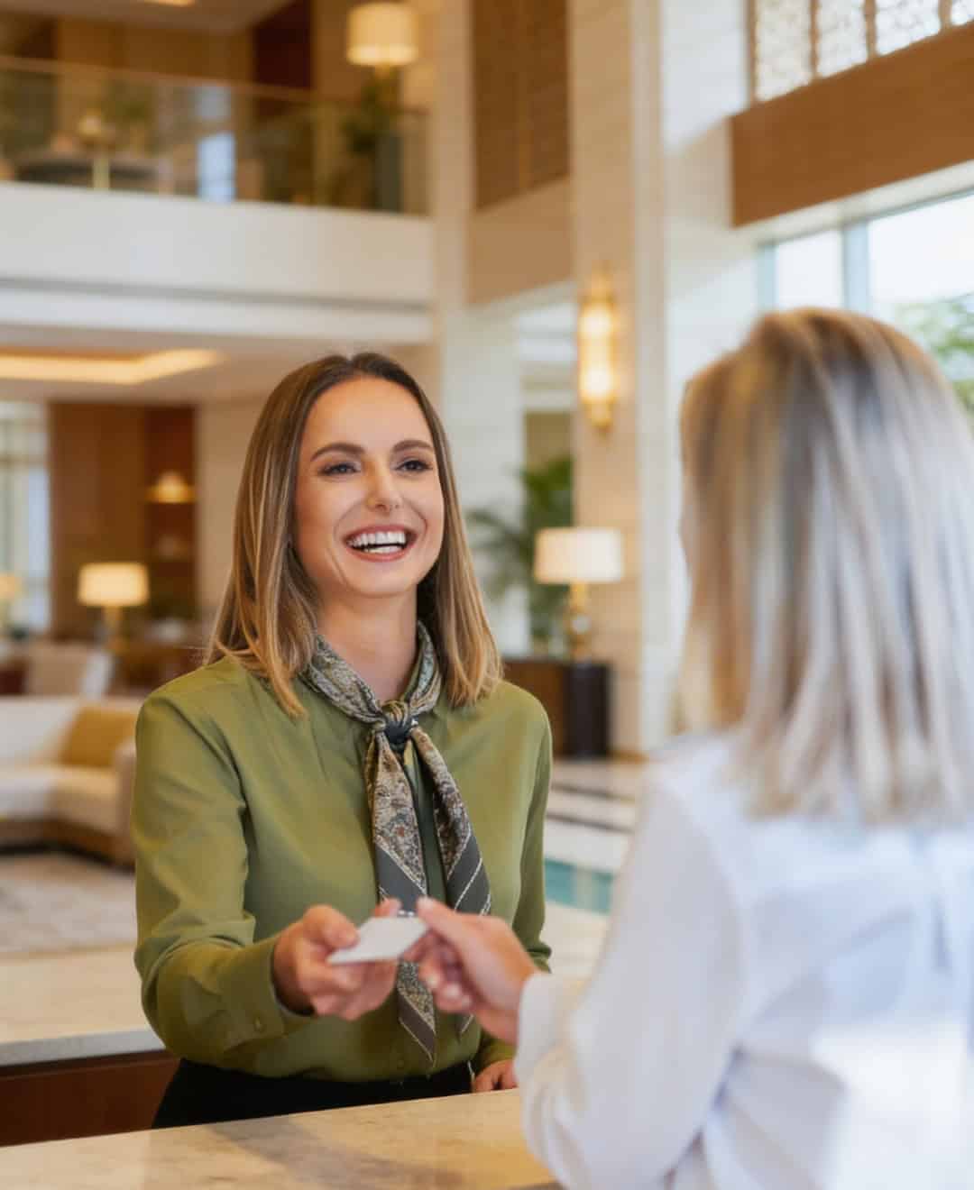 A woman smiling and handing a key card to a guest at a hotel reception desk, illustrating excellent guest service in a hospitality setting.