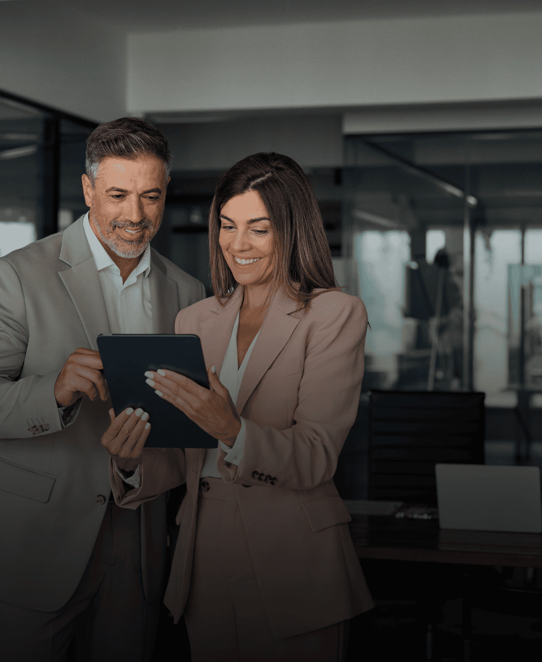 Two business professionals in a modern office looking at a tablet and discussing information with a positive, collaborative expression